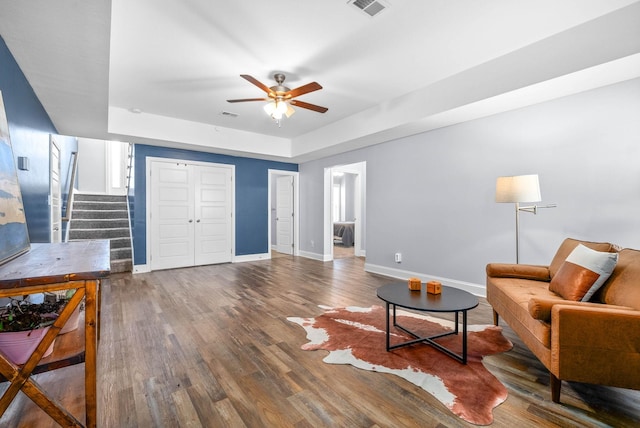 living room with ceiling fan, a tray ceiling, and hardwood / wood-style floors