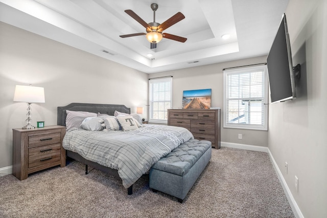 bedroom featuring ceiling fan, carpet, a tray ceiling, and multiple windows