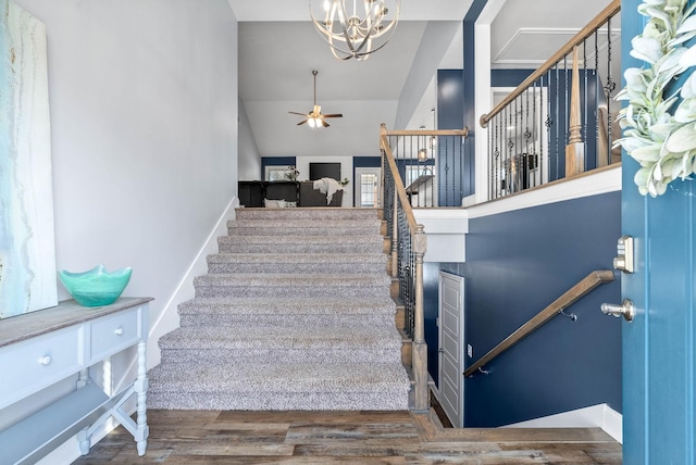 stairs featuring lofted ceiling, ceiling fan with notable chandelier, and hardwood / wood-style floors