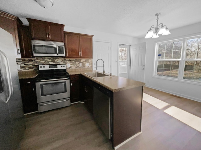 kitchen with stainless steel appliances, sink, decorative light fixtures, hardwood / wood-style flooring, and a notable chandelier