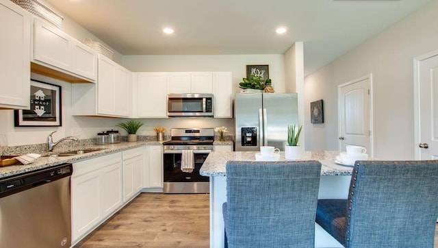 kitchen featuring white cabinets, stainless steel appliances, light wood-type flooring, and light stone countertops