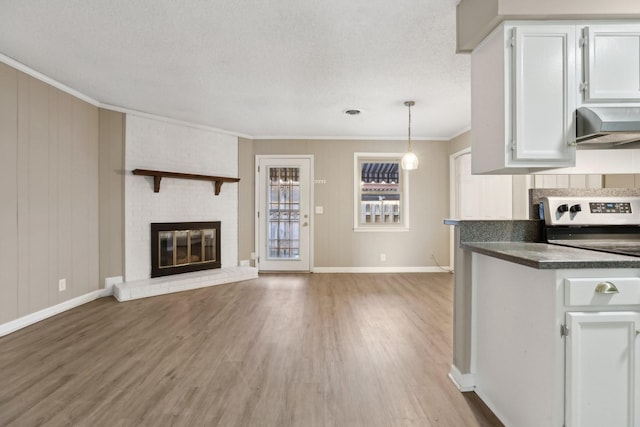 kitchen featuring a brick fireplace, pendant lighting, wood-type flooring, crown molding, and white cabinets