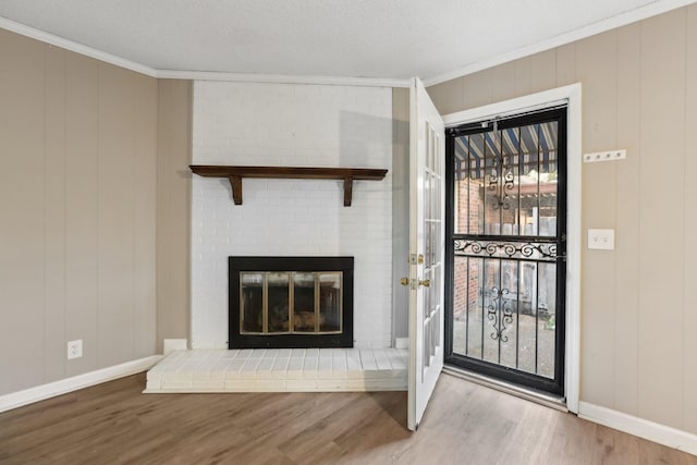 unfurnished living room with a textured ceiling, a brick fireplace, ornamental molding, and light hardwood / wood-style floors