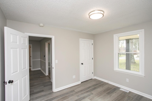 unfurnished bedroom with a textured ceiling, dark hardwood / wood-style flooring, and a closet