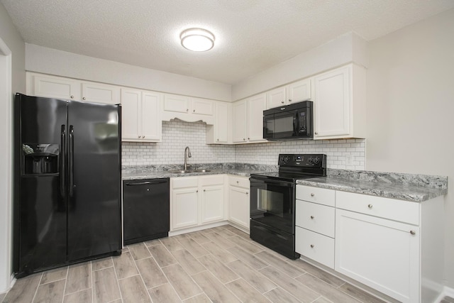 kitchen with light stone counters, a textured ceiling, black appliances, white cabinets, and sink