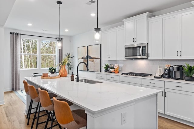 kitchen with sink, white cabinets, hanging light fixtures, a kitchen island with sink, and appliances with stainless steel finishes