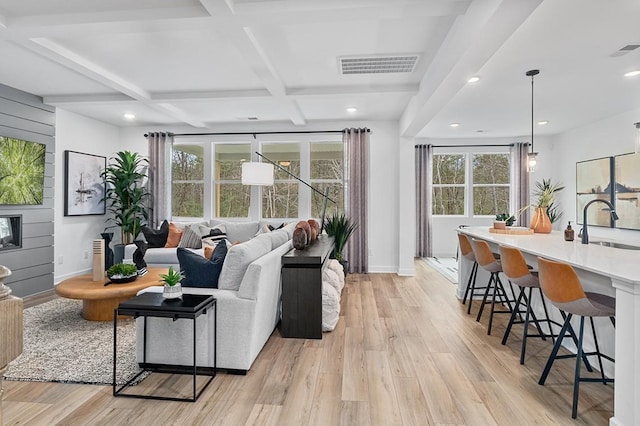 living room with coffered ceiling, sink, light wood-type flooring, and a healthy amount of sunlight