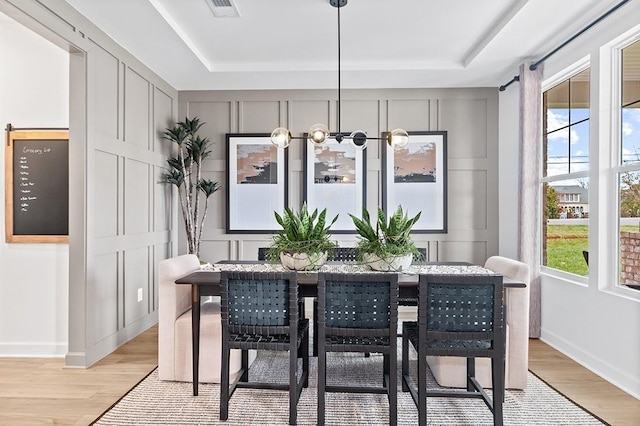 dining room featuring light hardwood / wood-style floors, a healthy amount of sunlight, and a tray ceiling