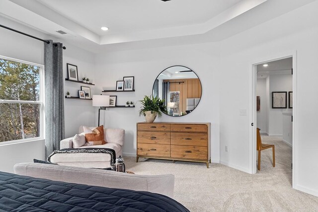 bedroom with a raised ceiling, light carpet, and multiple windows