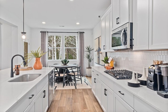 kitchen with sink, decorative light fixtures, white cabinets, light stone countertops, and appliances with stainless steel finishes