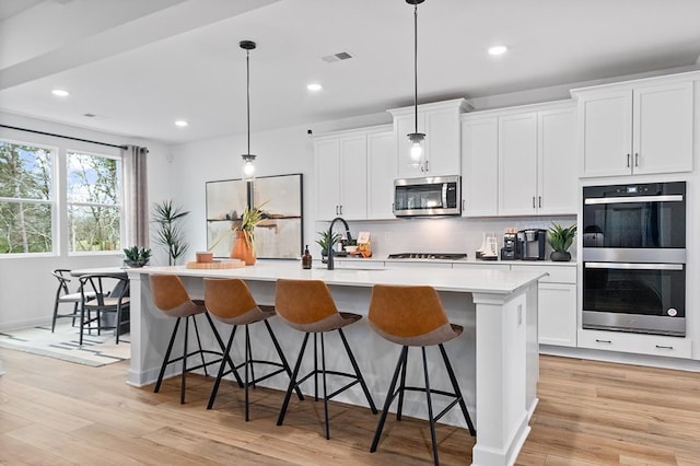 kitchen featuring hanging light fixtures, a kitchen island with sink, white cabinetry, appliances with stainless steel finishes, and sink