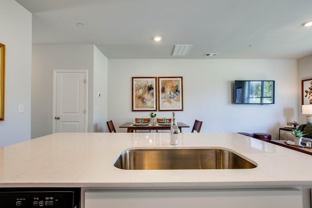 kitchen with sink, a kitchen island with sink, black dishwasher, and light stone countertops