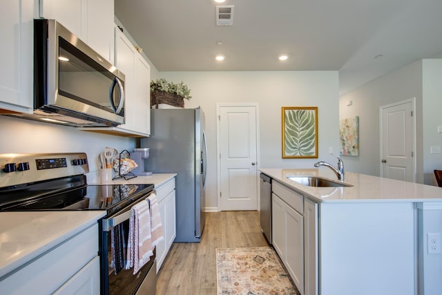 kitchen with stainless steel appliances, white cabinetry, sink, and an island with sink