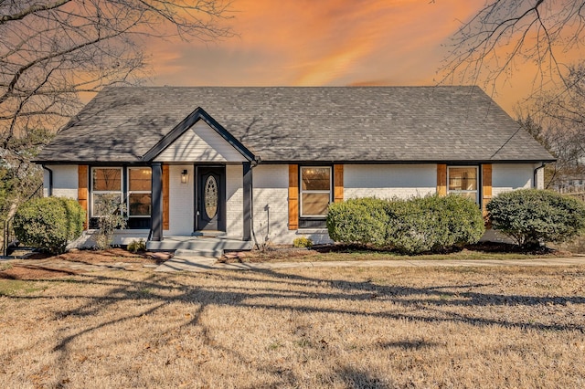 view of front of home with a front yard, brick siding, and roof with shingles