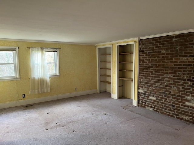 unfurnished bedroom with two closets, crown molding, light colored carpet, and brick wall