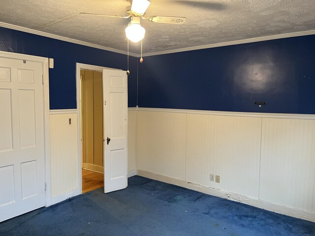 unfurnished bedroom featuring ceiling fan, ornamental molding, a textured ceiling, and dark colored carpet