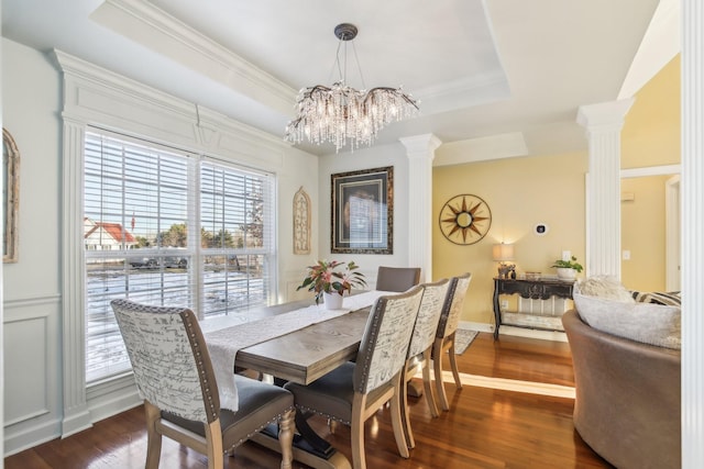 dining area featuring decorative columns, dark wood-type flooring, a tray ceiling, and a chandelier