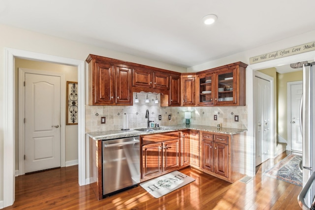 kitchen with hardwood / wood-style floors, appliances with stainless steel finishes, light stone counters, decorative backsplash, and sink