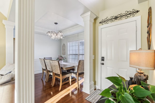 dining area featuring decorative columns, ornamental molding, wood-type flooring, a chandelier, and a tray ceiling