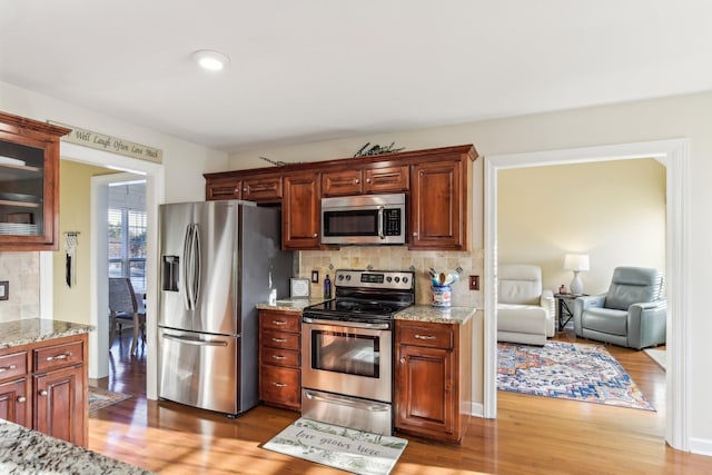 kitchen with light stone counters, stainless steel appliances, light hardwood / wood-style floors, and tasteful backsplash