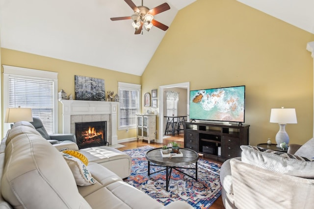 living room featuring high vaulted ceiling, a tiled fireplace, ceiling fan, and hardwood / wood-style flooring