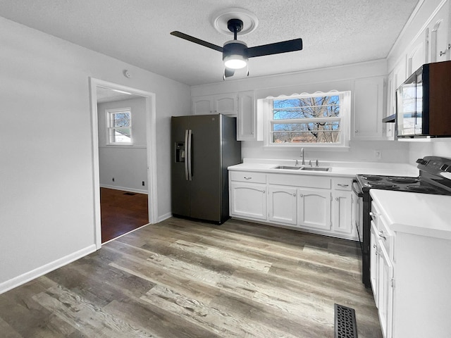 kitchen with stainless steel fridge, light hardwood / wood-style floors, black range with electric cooktop, white cabinetry, and sink