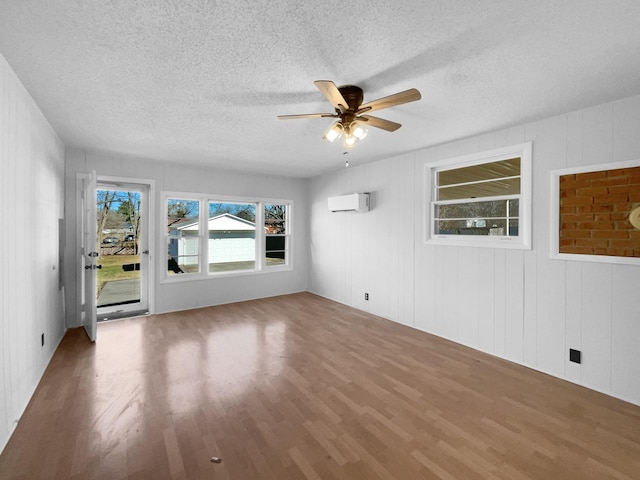 empty room featuring a textured ceiling, ceiling fan, a wall unit AC, and wood-type flooring