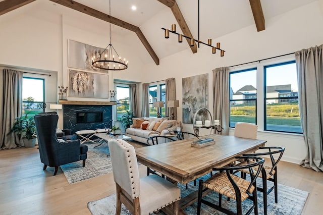 dining space featuring light hardwood / wood-style flooring, a premium fireplace, an inviting chandelier, high vaulted ceiling, and beamed ceiling