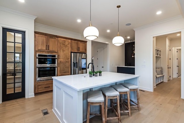 kitchen with a breakfast bar, appliances with stainless steel finishes, a kitchen island with sink, light hardwood / wood-style floors, and decorative light fixtures