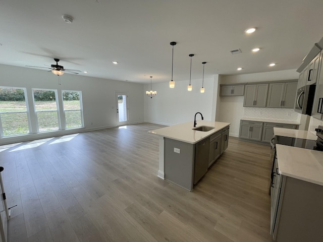 kitchen with a center island with sink, stainless steel appliances, decorative backsplash, sink, and ceiling fan with notable chandelier