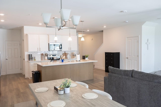 kitchen featuring hanging light fixtures, stainless steel appliances, an island with sink, white cabinets, and sink