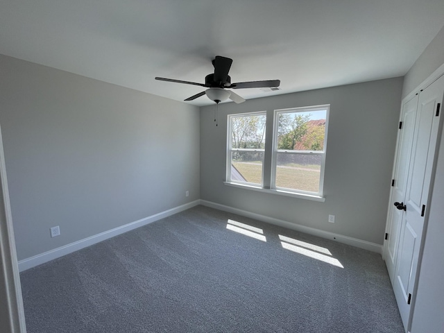 spare room with ceiling fan and dark colored carpet