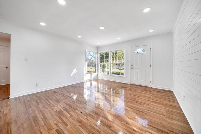 foyer entrance with brick wall, ornamental molding, and light hardwood / wood-style flooring