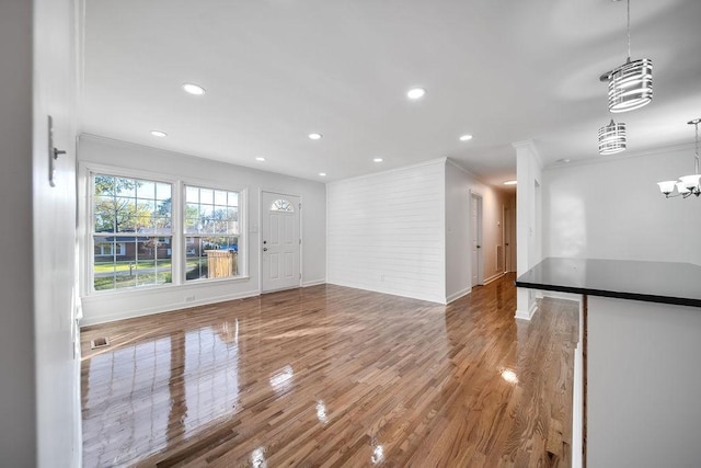 unfurnished living room featuring an inviting chandelier, crown molding, and hardwood / wood-style flooring