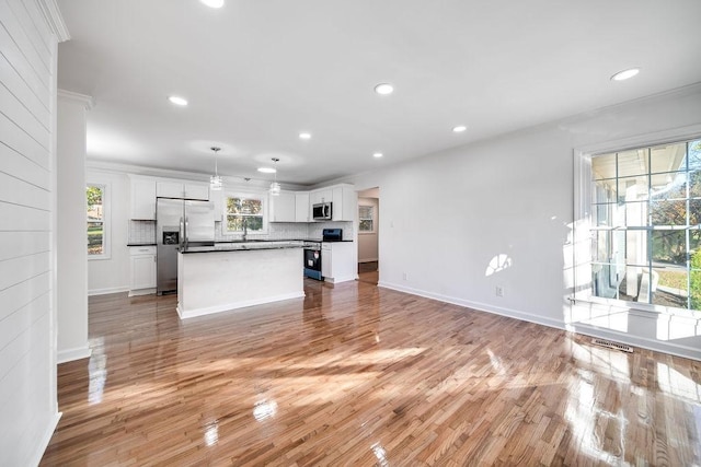 kitchen featuring appliances with stainless steel finishes, hanging light fixtures, a kitchen island, white cabinetry, and tasteful backsplash