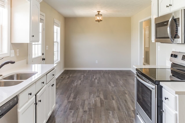 kitchen featuring stainless steel appliances, sink, white cabinetry, dark hardwood / wood-style floors, and pendant lighting