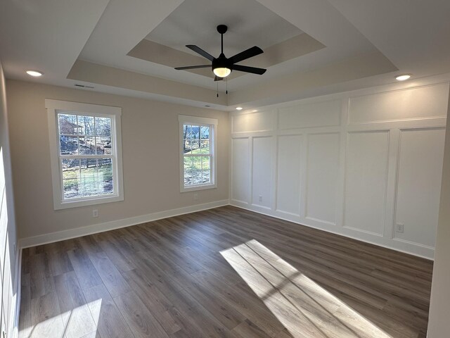 empty room with a wealth of natural light, a raised ceiling, ceiling fan, and dark hardwood / wood-style flooring