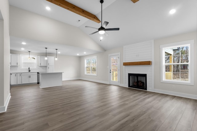 unfurnished living room with ceiling fan, hardwood / wood-style floors, vaulted ceiling with beams, a large fireplace, and sink