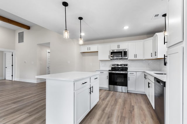 kitchen with stainless steel appliances, a kitchen island, pendant lighting, beam ceiling, and white cabinets