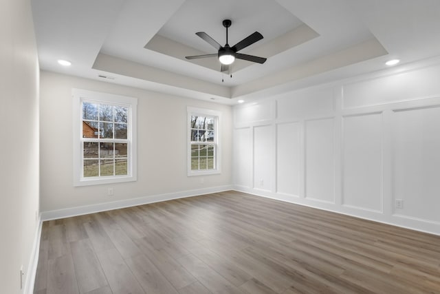 empty room featuring ceiling fan, wood-type flooring, and a raised ceiling