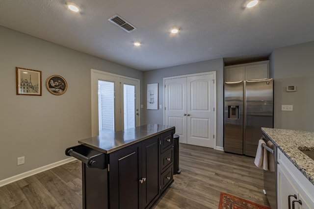 kitchen with light stone countertops, a textured ceiling, wood-type flooring, white cabinetry, and stainless steel appliances