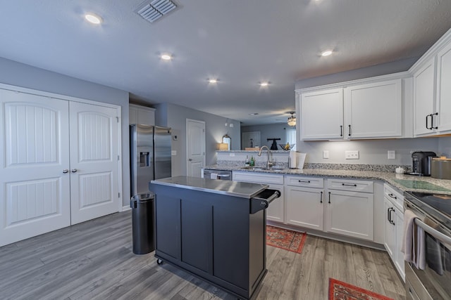 kitchen with appliances with stainless steel finishes, a center island, white cabinetry, light wood-type flooring, and ceiling fan