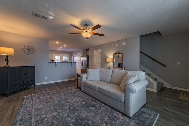 living room with a textured ceiling, dark wood-type flooring, and ceiling fan