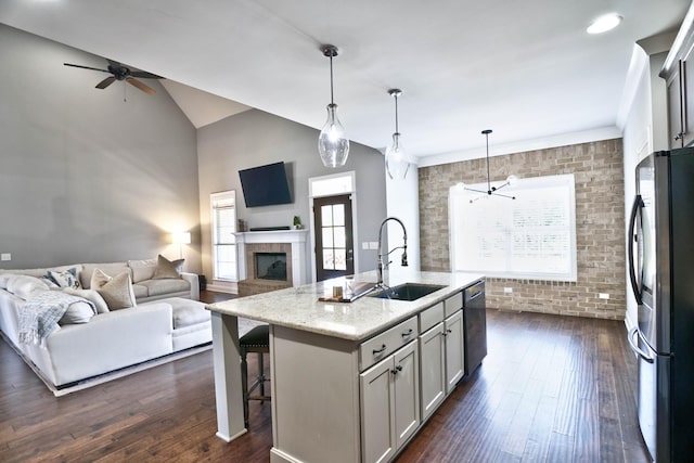 kitchen with light stone countertops, pendant lighting, a kitchen island with sink, appliances with stainless steel finishes, and sink