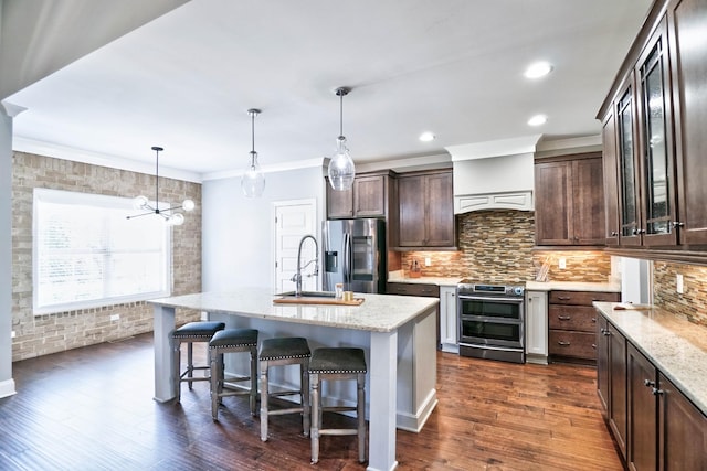 kitchen with light stone counters, a breakfast bar, a kitchen island with sink, appliances with stainless steel finishes, and dark brown cabinetry