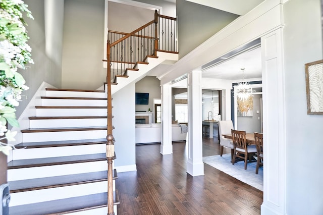 staircase with ornate columns, an inviting chandelier, and hardwood / wood-style flooring