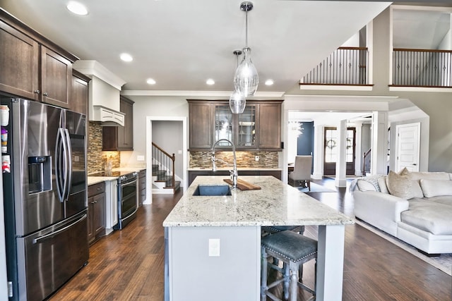 kitchen with stainless steel appliances, sink, decorative backsplash, dark brown cabinetry, and a center island with sink