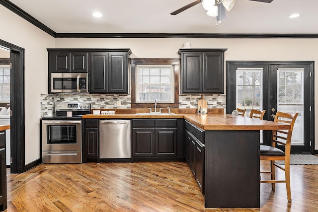 kitchen with light hardwood / wood-style floors, a kitchen bar, backsplash, appliances with stainless steel finishes, and sink