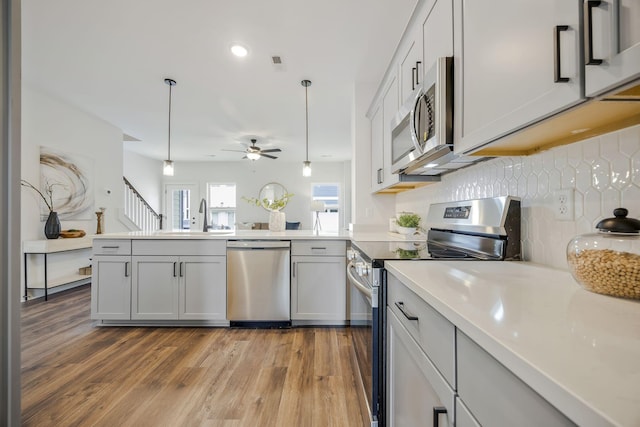 kitchen featuring pendant lighting, appliances with stainless steel finishes, sink, light wood-type flooring, and ceiling fan