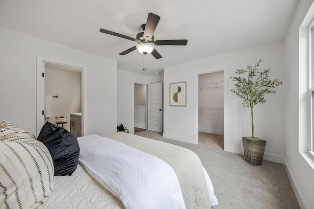 bedroom with a spacious closet, light carpet, ensuite bathroom, ceiling fan, and a closet